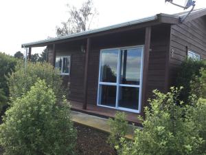 a log cabin with a large window and bushes at Kairaki Beach Motor Camp in Wetheral