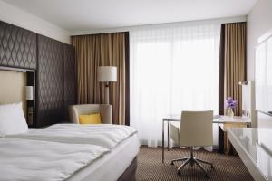 a hotel room with a bed, desk, chair and a lamp at Pullman Berlin Schweizerhof in Berlin