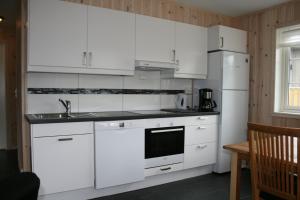 cocina con armarios blancos, fregadero y nevera en Tråsåvika Camping en Viggja