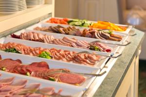 a buffet with several trays of meats and vegetables at Hotel am Schlosspark in Gotha