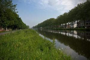a river with grass and buildings on the side at aan de vaart in Mechelen