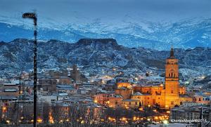 a city with a clock tower and a town with snow covered mountains at Hotel Palacio de Oñate in Guadix