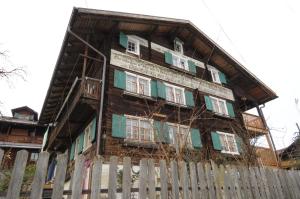 ein altes Holzhaus mit grünen Fenstern und einem Zaun in der Unterkunft BnB Hasatrog Jenaz in Jenaz