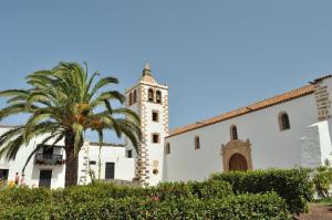 a building with a clock tower and a palm tree at El Aceitun Beach Holiday Homes in Gran Tarajal