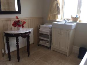 a bathroom with a sink and a table with flowers on it at Scarlett Rose Cottage in Cookstown