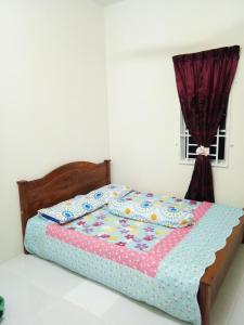 a bed in a white room with a bedspread and a window at Homestay AZMI ZITA in Kuala Terengganu