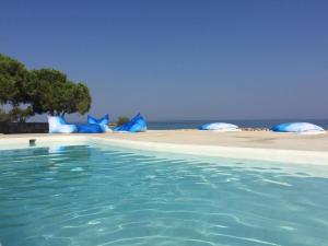 ein Pool neben einem Strand mit blauen Sonnenschirmen in der Unterkunft Eight Dimensions Capari Suites Elafonisos in Elafonisos