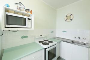 a white kitchen with a microwave and a stove at Ebbtide 7 in Forster +6 photos