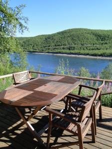 a wooden table and chairs on a deck with a river at Tenon näköalamökit in Utsjoki