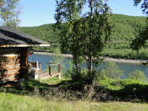 eine Blockhütte neben einem Fluss mit einem Baum in der Unterkunft Tenon näköalamökit in Utsjoki