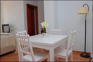 Una mesa blanca con tres sillas y un jarrón de flores. en Apartamento Conil con terraza, en Conil de la Frontera