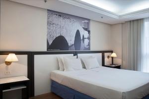 ポルト・アレグレにあるMaster Grande Hotel - Centro Históricoの白い大型ベッドが備わるベッドルーム1室、壁に絵画が飾られています。