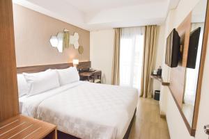una camera d'albergo con letto bianco e TV di Golden Tulip Essential Tangerang a Tangerang