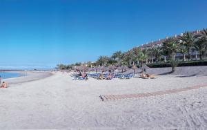a beach with people sitting in chairs and umbrellas at Hotel Cleopatra Palace in Playa de las Americas