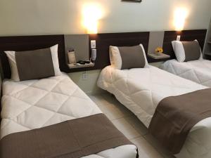 um quarto de hotel com duas camas com lençóis brancos em Hotel do Reinildo I em Cachoeira Paulista