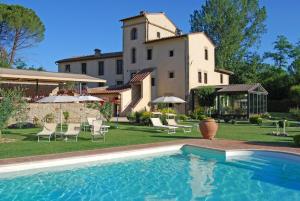 
a large white house with a pool and lawn chairs at Molino Di Foci in San Gimignano
