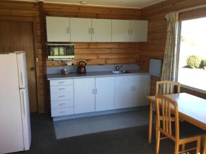 a kitchen with white cabinets and a table and a refrigerator at Kairaki Beach Motor Camp in Wetheral