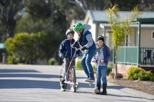 three children riding skateboards down a street at Riverside Cabin Park in Shepparton