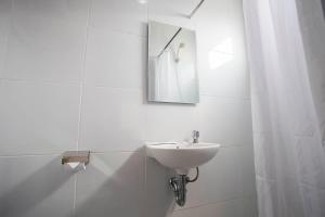 ein weißes Badezimmer mit einem Waschbecken und einem Spiegel in der Unterkunft De Green Inn @aeropolis in Tangerang