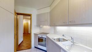 a kitchen with white cabinets and a sink and a hallway at La Planüra 15 in Maloja