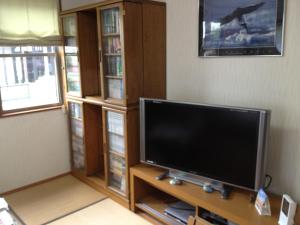 a living room with a flat screen tv and book shelves at Beppu Yukemuri-no-oka Youth Hostel in Beppu