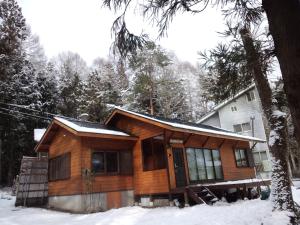 uma cabana de madeira na neve em frente a uma casa em Kamoshika Cottage Hakuba em Hakuba