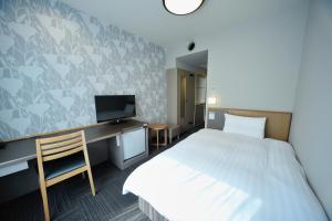 a bedroom with a bed and a desk with a television at Dormy Inn Chiba City Soga in Chiba