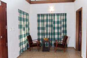 Zimmer mit 2 Stühlen und einem Tisch mit einem grünen und weißen Vorhang in der Unterkunft Century Village Resort in Mananthavady