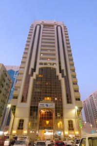 wysoki budynek z samochodami zaparkowanymi przed nim w obiekcie Ivory Hotel Apartments w Abu Zabi