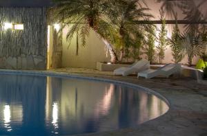 a swimming pool with white loungers and a palm tree at Hotel Morada das Águas in Caldas Novas