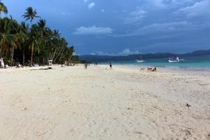 a sandy beach with people and a boat in the water at Blue Coral Resort Boracay in Boracay
