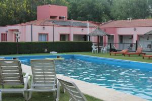 a swimming pool with chairs and a pink building at Piscoyaku Apart-Amplio parque con cancha de padel, voley y futbol in Potrero de los Funes