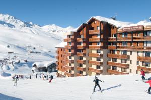 a group of people skiing in the snow in front of a hotel at Résidence Le Chamois d'Or in Val Thorens