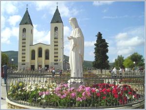 a statue of a god in front of a church with flowers at Guesthouse Soče in Međugorje