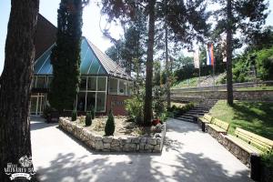 ein Gebäude mit Bäumen und Bänken davor in der Unterkunft Garni Hotel Mlinarev san in Arilje