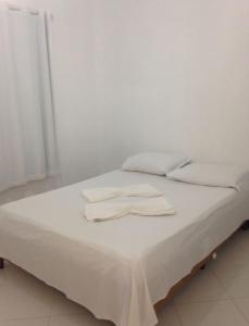 Una cama blanca con dos toallas blancas encima. en CHALÉS ENCANTOS DA ILHA, en Barra dos Coqueiros