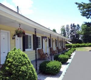 a yellow house with a porch with chairs and bushes at Weathervane Motel Lanesboro in Lanesborough