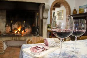two glasses of wine and cheese on a table with a fireplace at Il Cielo in Terra: Il Podere in Montaione