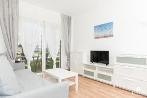 a white living room with a white couch and a tv at Jantar Apartamenty - Pod Lipami in Kołobrzeg