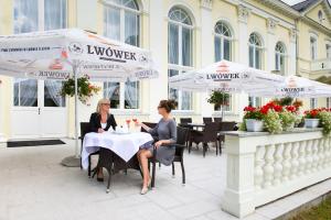 zwei Frauen sitzen an einem Tisch unter Sonnenschirmen in der Unterkunft Uzdrowisko Cieplice - Jelenia Góra - Pawilon Edward in Jelenia Góra
