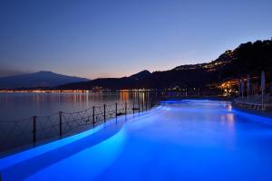 a swimming pool with blue lights in the water at night at UNA HOTELS Capotaormina in Taormina