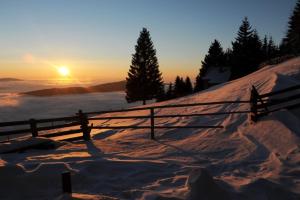 a fence on top of a snow covered hill with the sunset at Gartenwohnung auf der Sommeralm in Sankt Kathrein am Offenegg