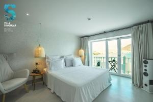a white bedroom with a bed and a chair at Villa Singular in San José