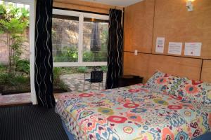 a bedroom with a bed with a colorful comforter and a window at Dolphins Backpackers in Sunshine Beach
