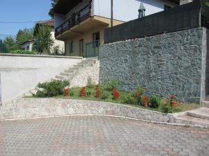 a stone retaining wall next to a building with flowers at Apartman Bilanovic in Konjic
