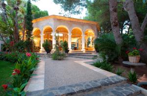 une grande maison avec une véranda ornée d'arbres et de fleurs dans l'établissement Lago Garden Apart-Suites & Spa Hotel, à Cala Ratjada