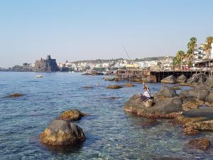 osoba siedząca na skałach w wodzie w obiekcie Apartment Inn w mieście Aci Castello