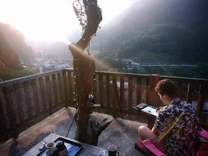 una mujer sentada en un balcón con vistas a una montaña en Experiencing Traditional Life Style Inn Kajiya Iya Romantei, en Miyoshi