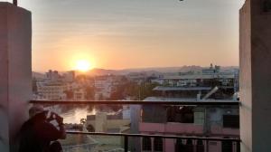 un hombre tomando una foto de la puesta de sol desde un balcón en Udai Haveli Guest House, en Udaipur