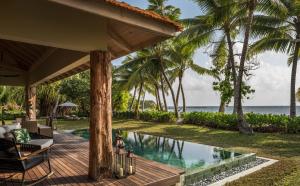 a resort pool with palm trees and the ocean at Four Seasons Resort Seychelles at Desroches Island in Desroches